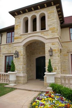 the front entrance to a large house with flowers in the foreground and potted plants on either side