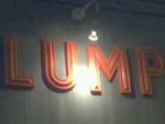 the sign for jump is lit up in bright orange letters on a white wall with a light bulb above it