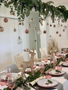 the table is set for christmas dinner with ornaments and greenery hanging from the ceiling