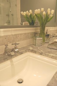 a bathroom sink with marble counter top and white tulips in front of the mirror