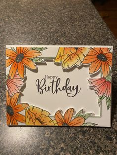 a happy birthday card with orange flowers on the front and bottom, sitting on a granite countertop