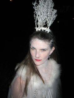 a woman wearing a tiara with branches on it's head and fur stole around her neck