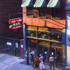 several people are standing outside of a bar on the sidewalk in front of a building