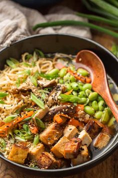 a bowl filled with noodles, vegetables and tofu on top of a wooden table