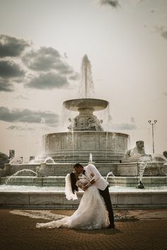 a bride and groom standing in front of a fountain