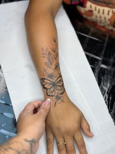 a woman's hand with a butterfly tattoo on her left arm and another person's wrist