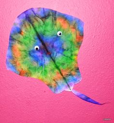 a colorful leaf with eyes on it hanging from a pink wall in front of a pink background