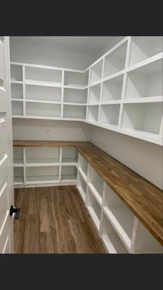 an empty walk in closet with white shelving and wood flooring