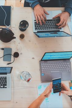 three people sitting at a table with laptops and cell phones in front of them