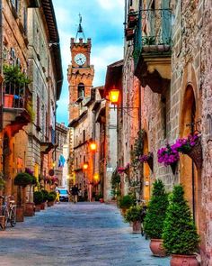 a clock tower is in the distance between two buildings on a street with potted plants