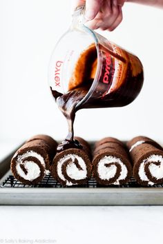 someone pouring chocolate sauce on top of some cake roll holes that are sitting on a cooling rack