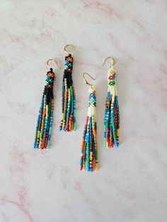 three pairs of multicolored beaded tassels hanging from hooks on a marble surface