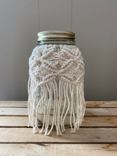 a mason jar with white yarn and tassels on the lid sitting on a wooden table