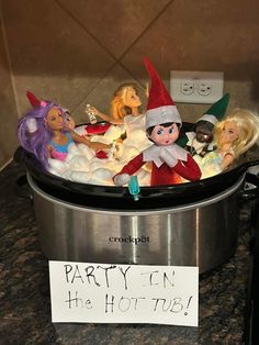 a pot full of dolls sitting on top of a counter next to a sign that says party in the hot tub