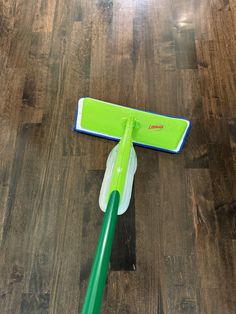 a green mop laying on top of a wooden floor next to a cleaning brush