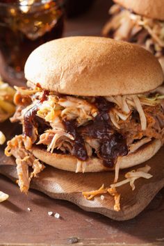 two pulled pork sandwiches sitting on top of a wooden cutting board