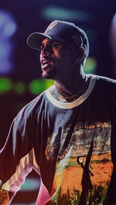 a man in a black hat and t - shirt holding a cell phone while standing on stage