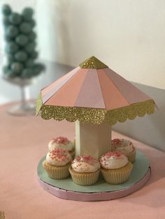 some cupcakes are sitting on a plate under a pink and gold umbrella with sprinkles