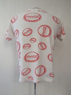 "Vintage 1970s(?) Coca Cola t-shirt. Made of white cotton with red all over bottle cap graphics Coka Cola. Pop art Coke advertising shirt. Made by Coka Cola. About a size large(one size fits all). Actual measurements are: 40\" around the chest 40\" around the waist 18\" shoulder seam to shoulder seam 24\" overall length In good condition with a faint spot on the front(photo)." Cola Bottle, Coca Cola Bottle, Diet Coke, Bottle Cap, Logo T Shirt, Vintage 1970s, Vintage Tshirts, Spot On, Coca Cola