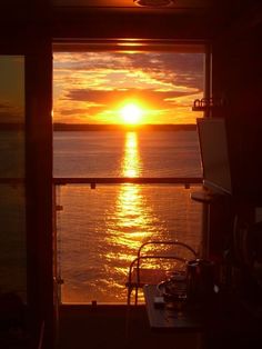 the sun is setting over the water from inside a room with an open door that leads to another room