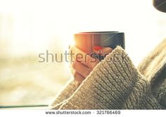 a woman holding a coffee cup in her hands and looking out the window with sunlight streaming through