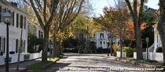 an empty street lined with white houses and trees in the fall time, during the day