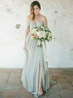 a woman standing in front of a white wall wearing a dress and holding a bouquet