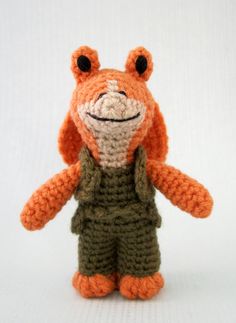 a crocheted orange stuffed animal wearing overalls and an army green shirt with black eyes