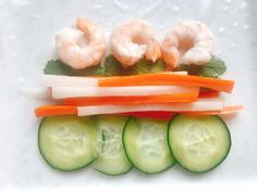 a white plate topped with cucumbers, carrots and shrimp on top of each other