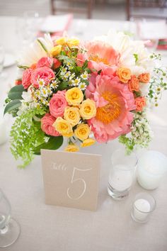 an arrangement of flowers on a table with candles and place cards for the guests to sit at