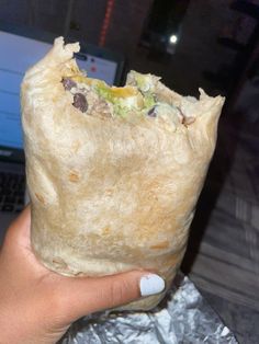 a hand holding a burrito in front of a laptop