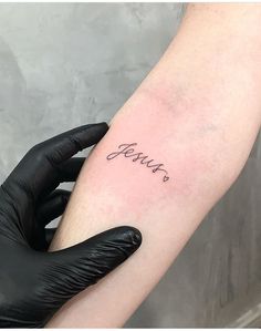 a person with a black glove on their arm holding a small tattoo that says jenny