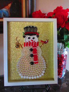 a snowman made out of pearls and beads on a table next to red roses