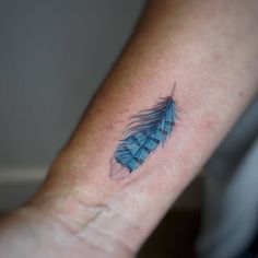 a small blue feather tattoo on the wrist