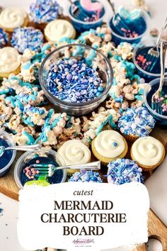 a wooden board topped with lots of blue and white decorated cupcakes next to a bowl of sprinkles