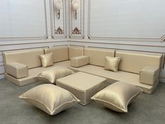 a couch with four pillows on it in front of a white wall and two chandeliers