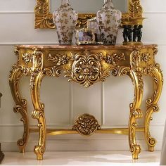 an ornate gold console table with two vases on top and a mirror above it