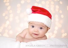 a baby wearing a santa hat laying on top of a white blanket with lights in the background