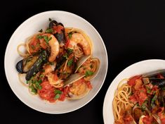 two white bowls filled with pasta and clams on top of a black table next to each other