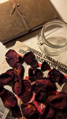 dried flowers on top of a newspaper next to a glass cup with water in it