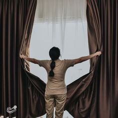 a woman standing in front of curtains with her hands on the curtain's edge