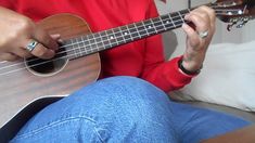 a person sitting on a couch playing an ukulele with their hands and fingers