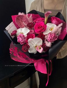 a woman holding a bouquet of pink and white flowers in front of a black table