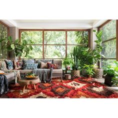 a living room filled with lots of furniture and plants on top of a red rug