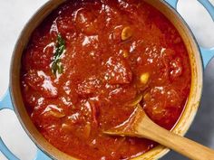 a pot filled with red sauce on top of a counter next to a wooden spoon