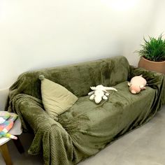 a couch covered in a green blanket next to a potted plant