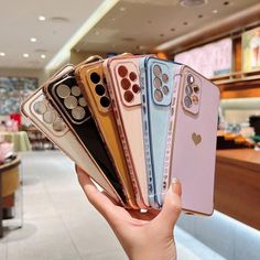 a person holding five different colored iphones in front of a store display with other models