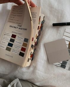 a person holding an open book on top of a bed next to paint swatches