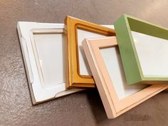 three different colored frames sitting next to each other on the floor in front of a wall