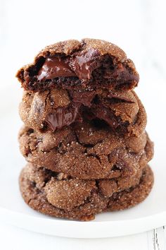 three chocolate cookies stacked on top of each other in front of a white plate with one cookie